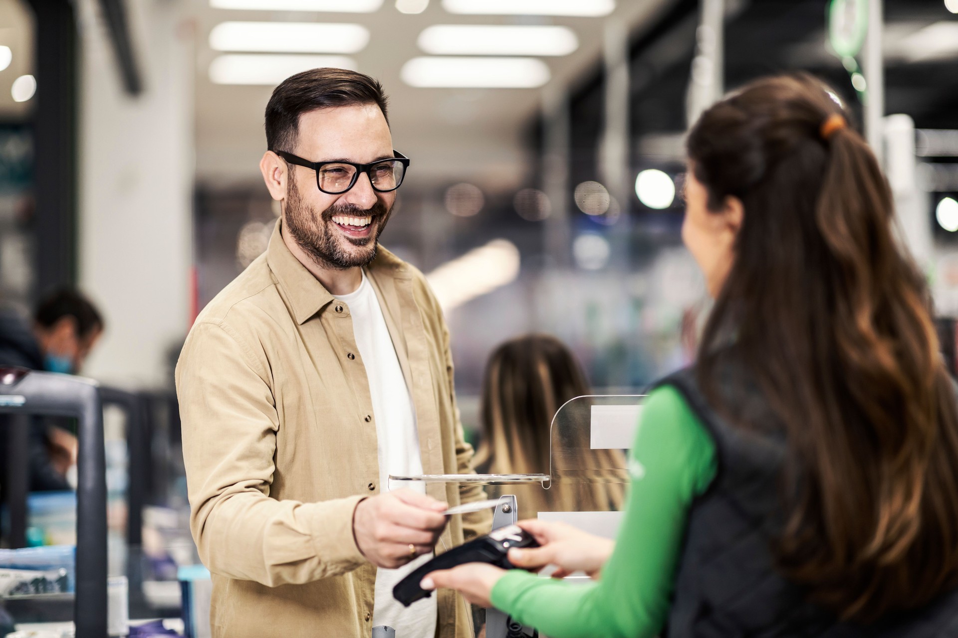 A happy customer paying at checkout with credit card in supermarket.